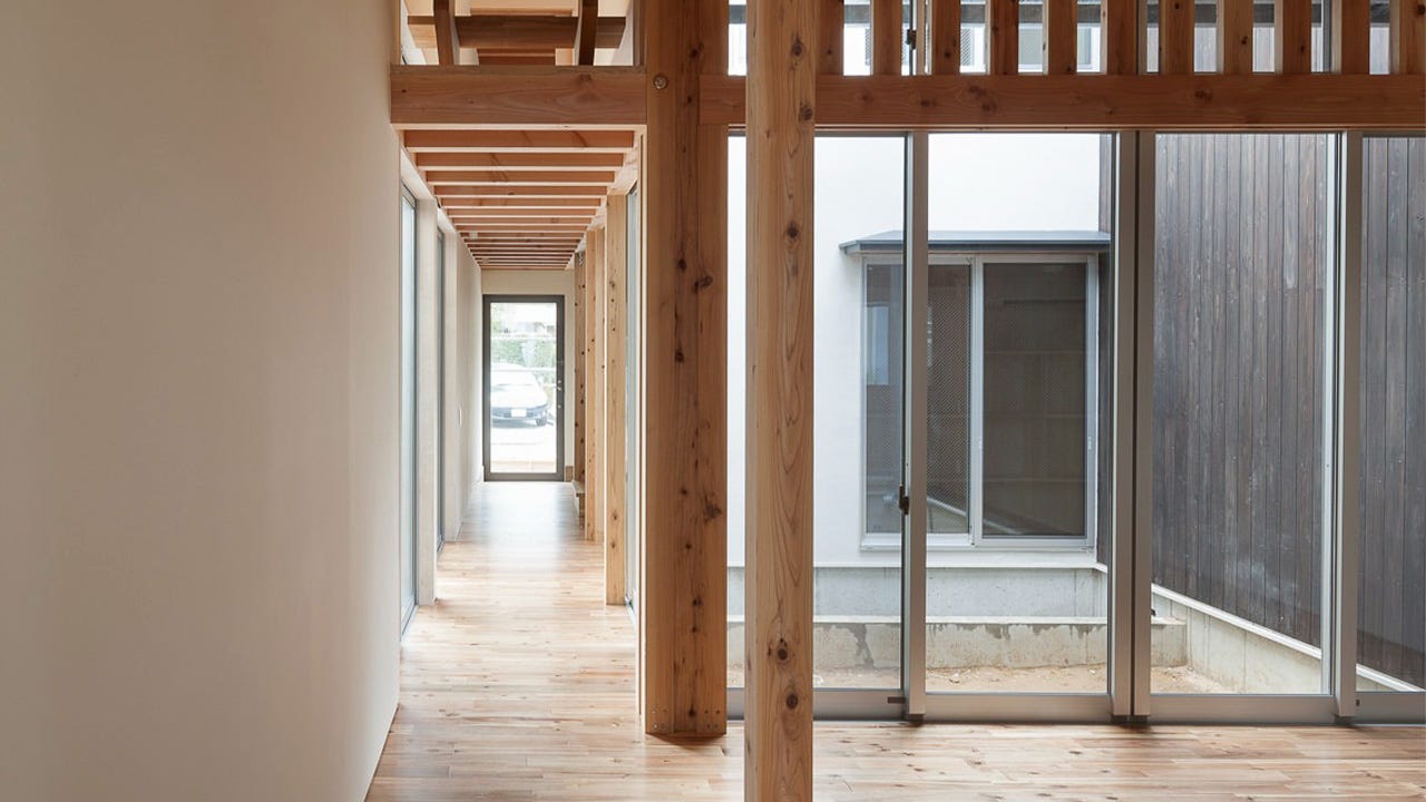 施工事例　府中の家 (天井を張らずに松の木で統一した梁が、長い廊下と中庭を引き立てます。中庭の大きな窓には、光と風を取り入れるスリットの門型フレームを構え、大きな窓を塞ぐことなく耐震性が高められています。)