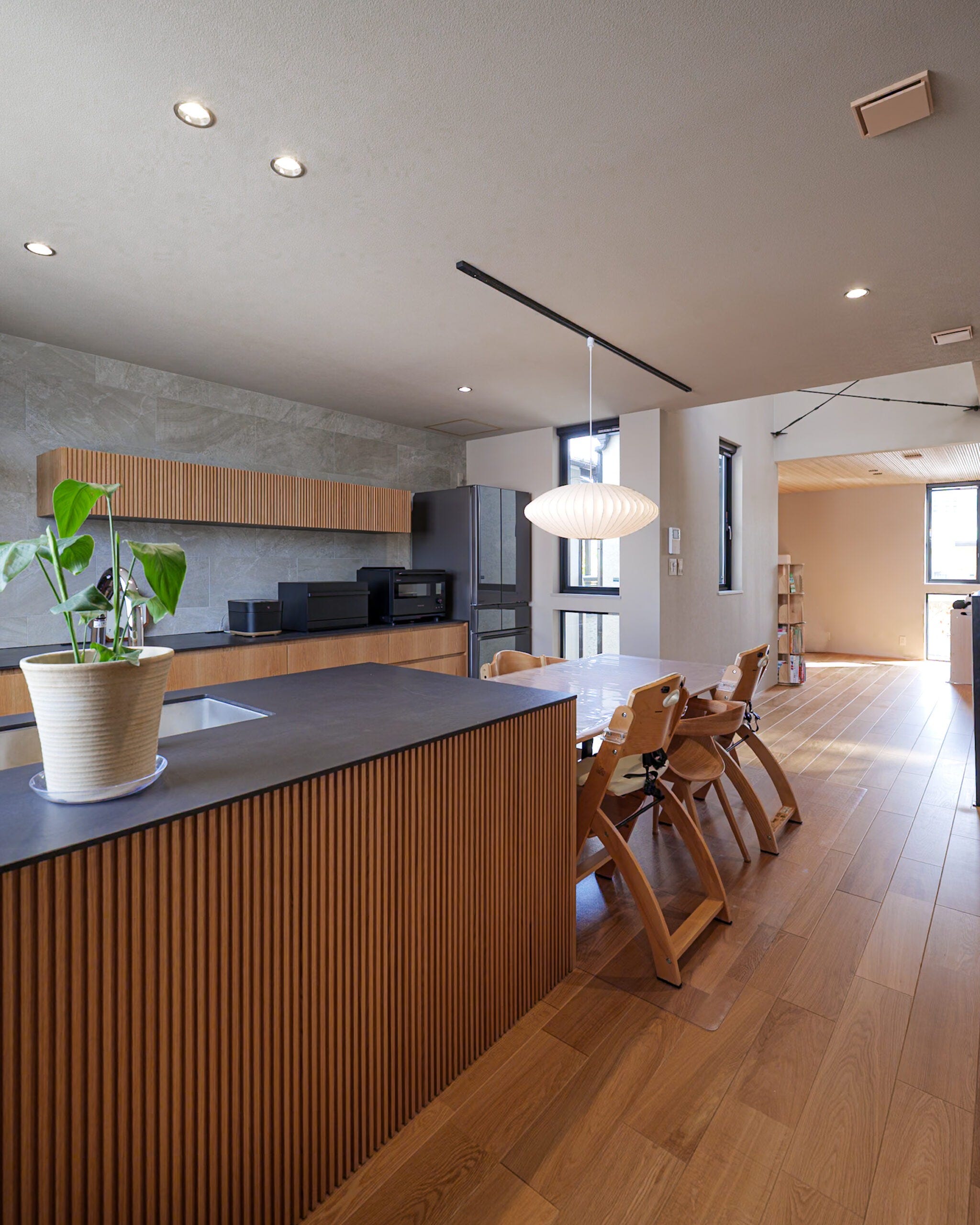 木の温もりとグレージュの落ち着きが調和したキッチン・ダイニング。縦格子のデザインが美しいキッチンカウンターが空間のアクセントとなり、上質で心地よい雰囲気を演出します。家族が自然と集まり、日常の会話がふくらむあたたかな空間です。