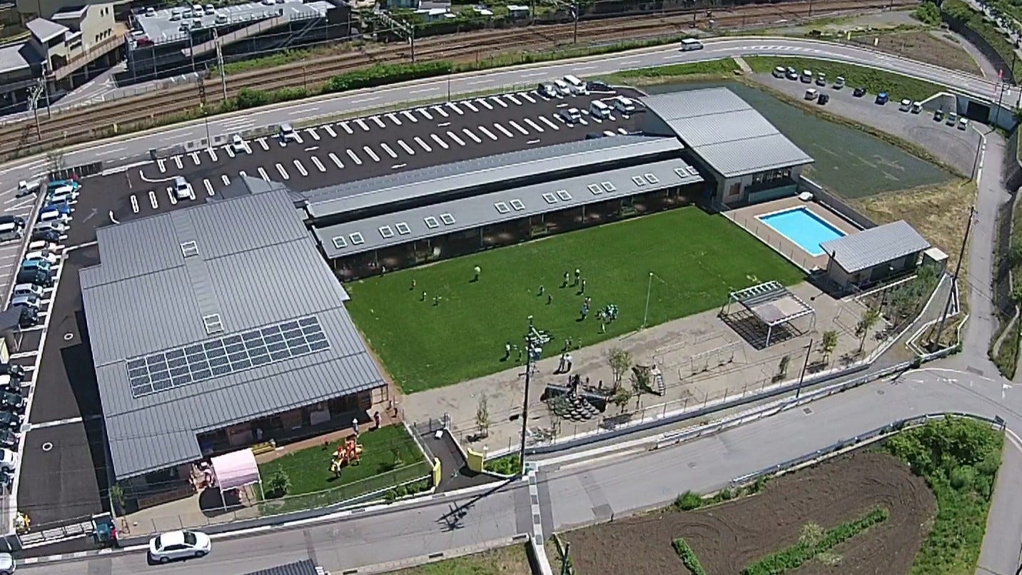 東御市立田中保育園 (長野県の東部、上田市や小諸市に隣接する東御市における市立保育園。指名プロポーザルでの最優秀賞選定を経ての建築となりました。敷地のある場所はしなの鉄道田中駅の南口から程ない場所にあり、南北に道路が走り、四周に開け、遠望に浅間山をはじめとした連なる山々が眺望できるロケーションです。そのような敷地において、敷地を最大限利用した木造平屋の建築、送迎用の駐車スペース、周囲からの安全性に配慮しながらも自然との触れ合いを重視し芝生の園庭が慎重に配置計画されました。園舎は長野県産材の木を多様したぬくもりのある内外部の空間の設えとし、外観は周囲に山野に呼応する伸びやかな曲面の大屋根を建築の象徴としています。)