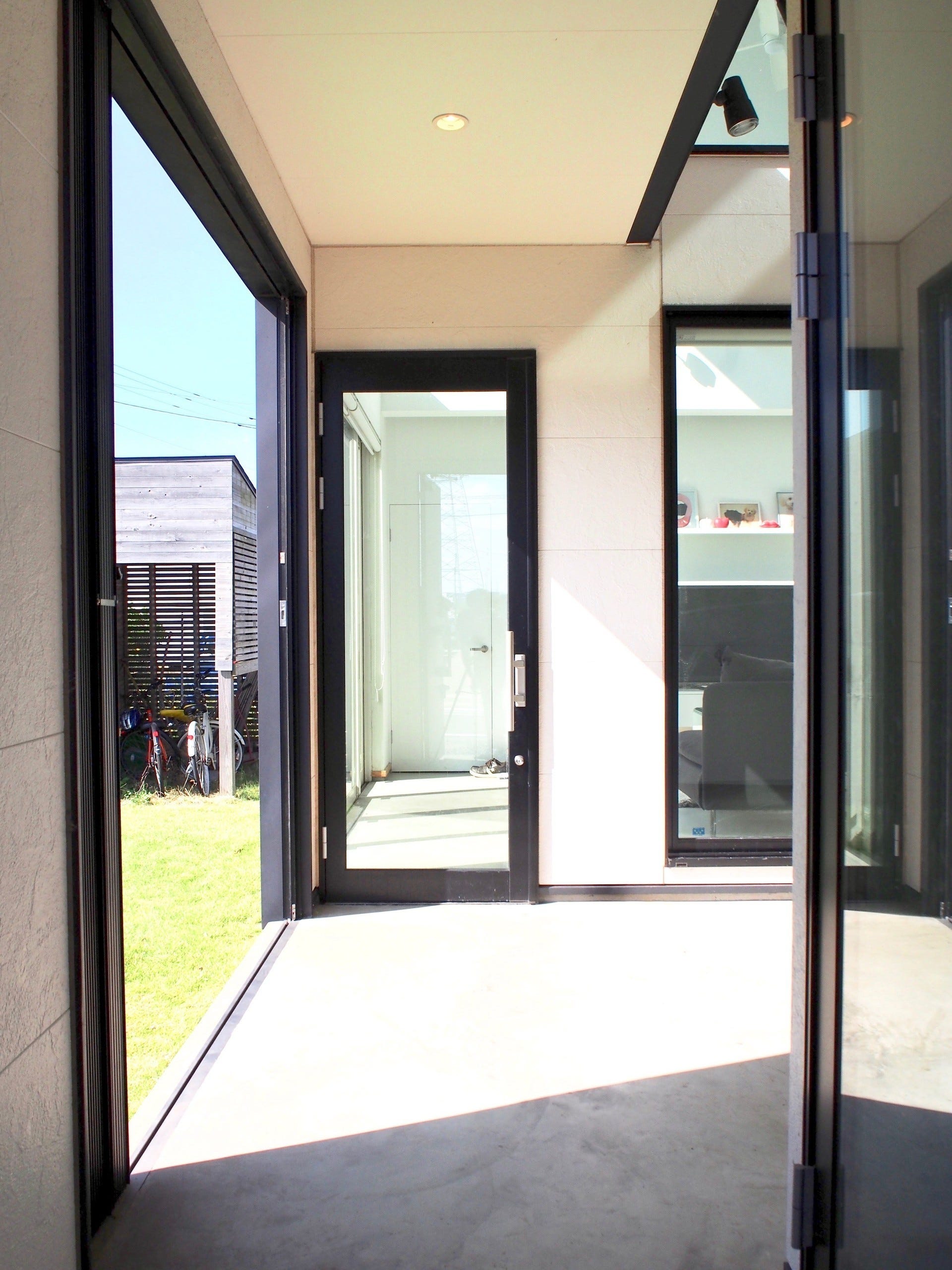 玄関ドアを開けると目の前に現れる空間は建物中央部分に設けた中庭となっており、そこは外部と接続された空間のため、内部であり外部である曖昧な空間となっている。
普段は閉じられた中庭として利用し、横引きシャッターを開けると今度は一気に外部に開放され、庭と建物が繋がった一体の空間として利用できるようになっている。